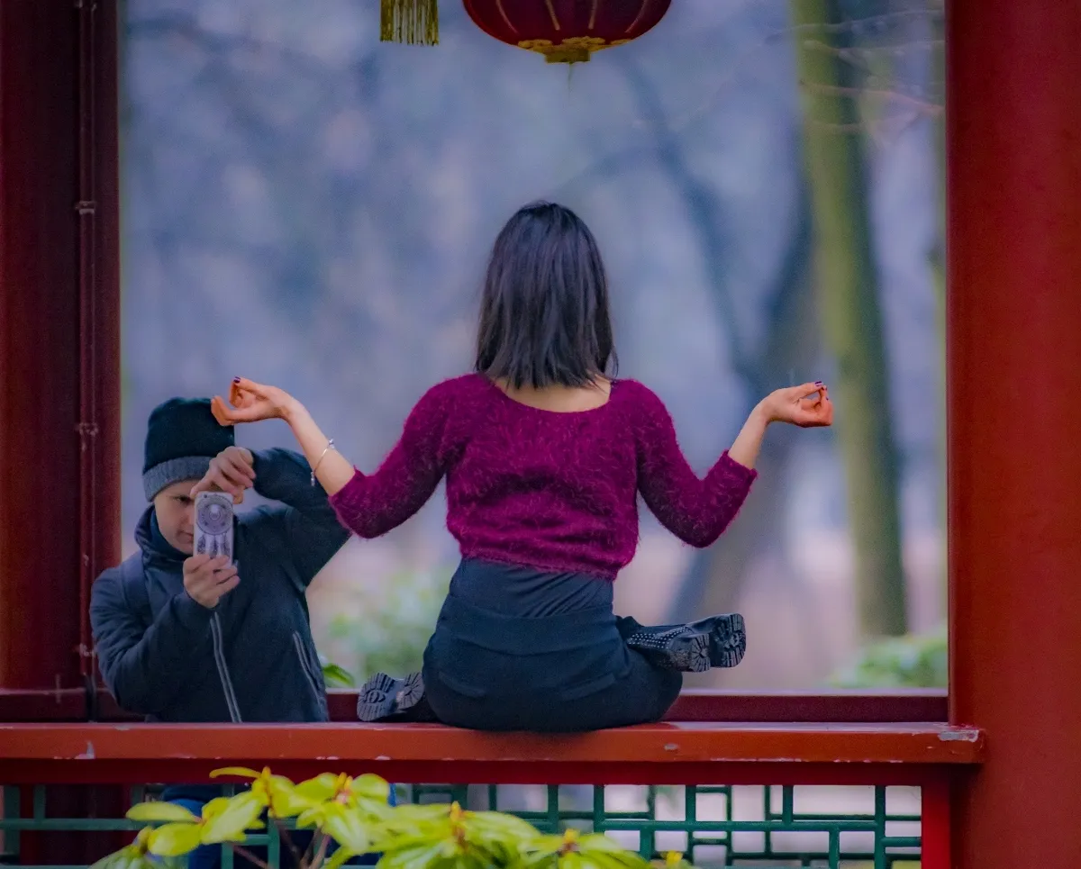 Child photographing a woman seated cross-legged inside a pavilion-like structure